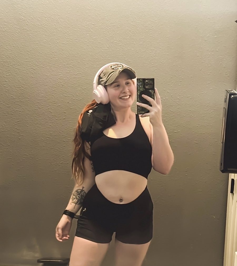 Taylor smiling in a gym mirror selfie with headphones and a cap